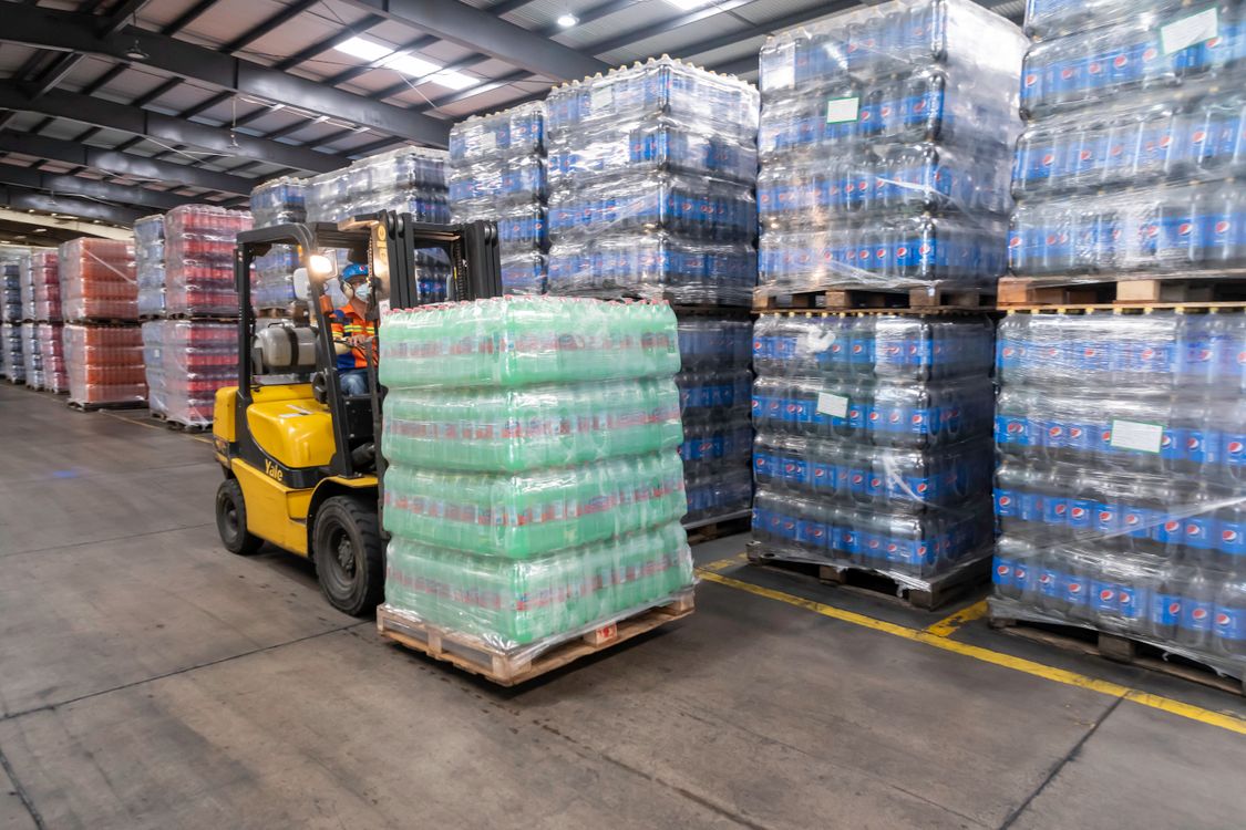 Montacargas operando entre pasillos de un almacen con pallets apilados