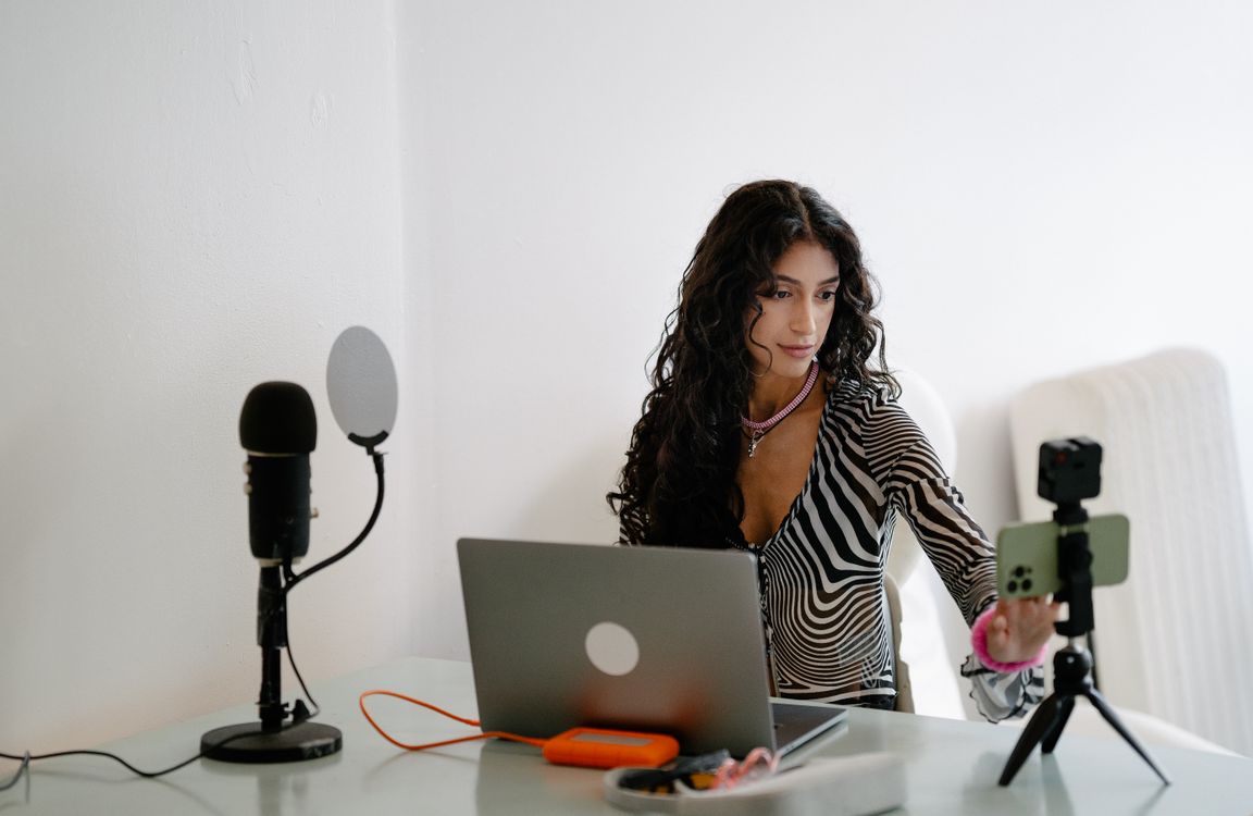 Woman livestreaming at desk with laptop and smartphone recording equipment