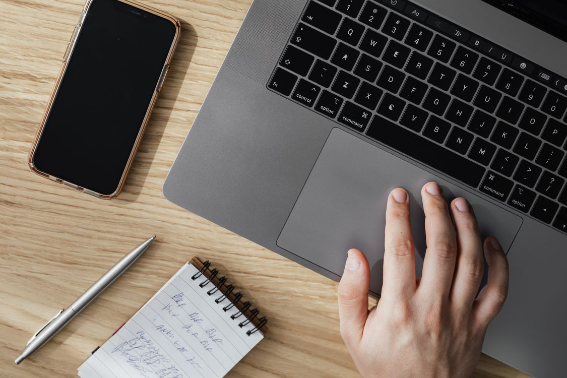 Content creator working on a laptop with a smartphone and notepad on a desk