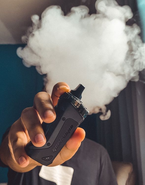 Persona sosteniendo un vape y exhalando una nube de vapor