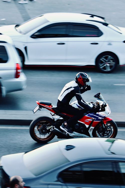 Motociclista com capacete trafegando entre carros em via urbana