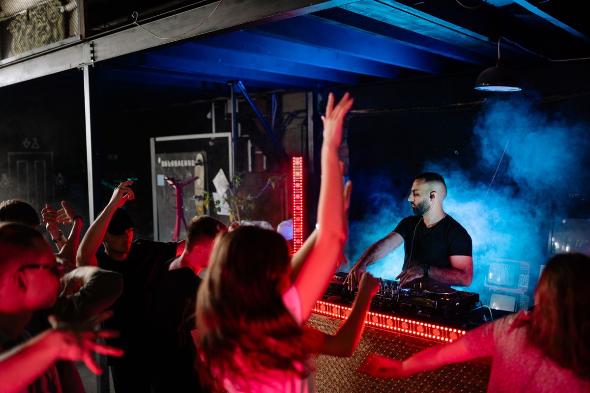 DJ performing at a mixing console with a lively nightclub crowd and vibrant lighting