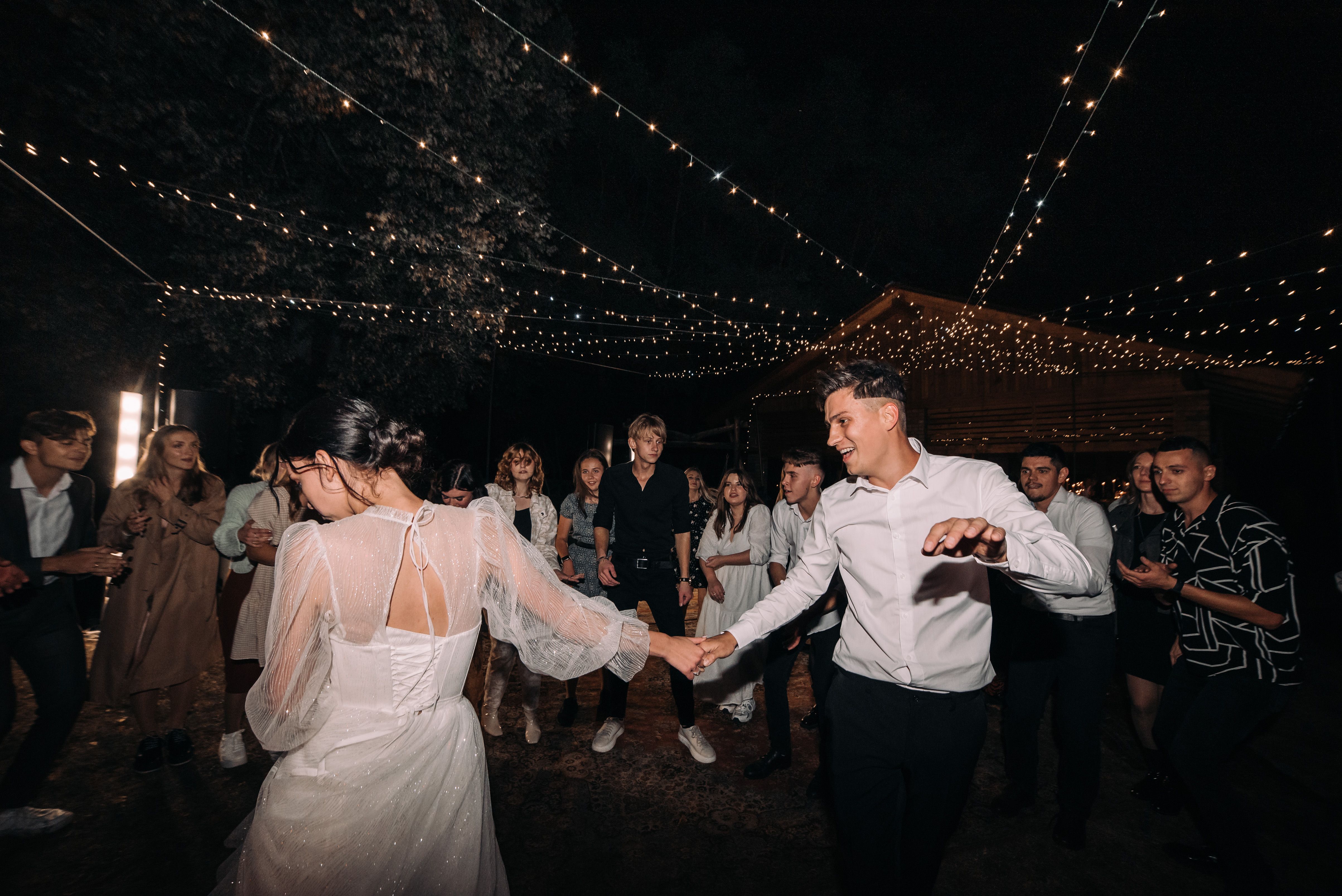 Newlywed couple dancing surrounded by celebrating guests under evening lights