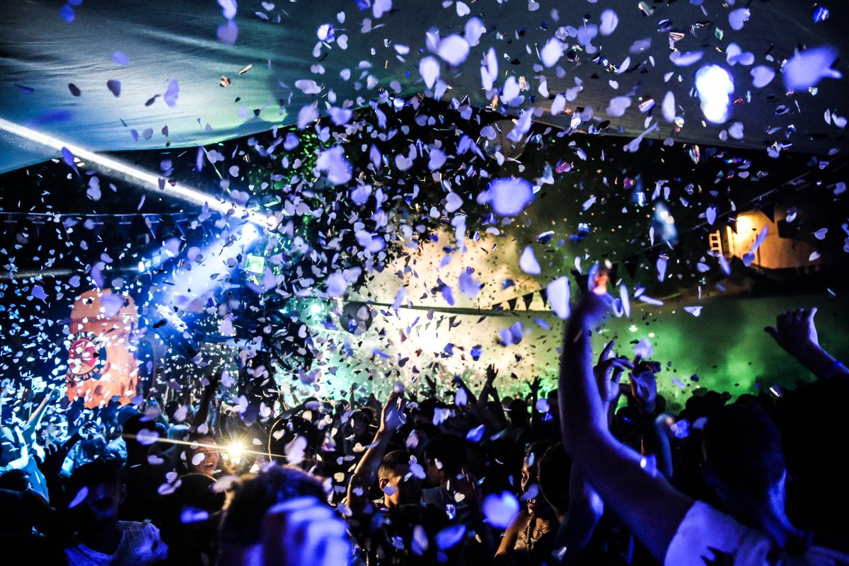 Crowd dancing under colorful lights at a nightclub rave with confetti falling