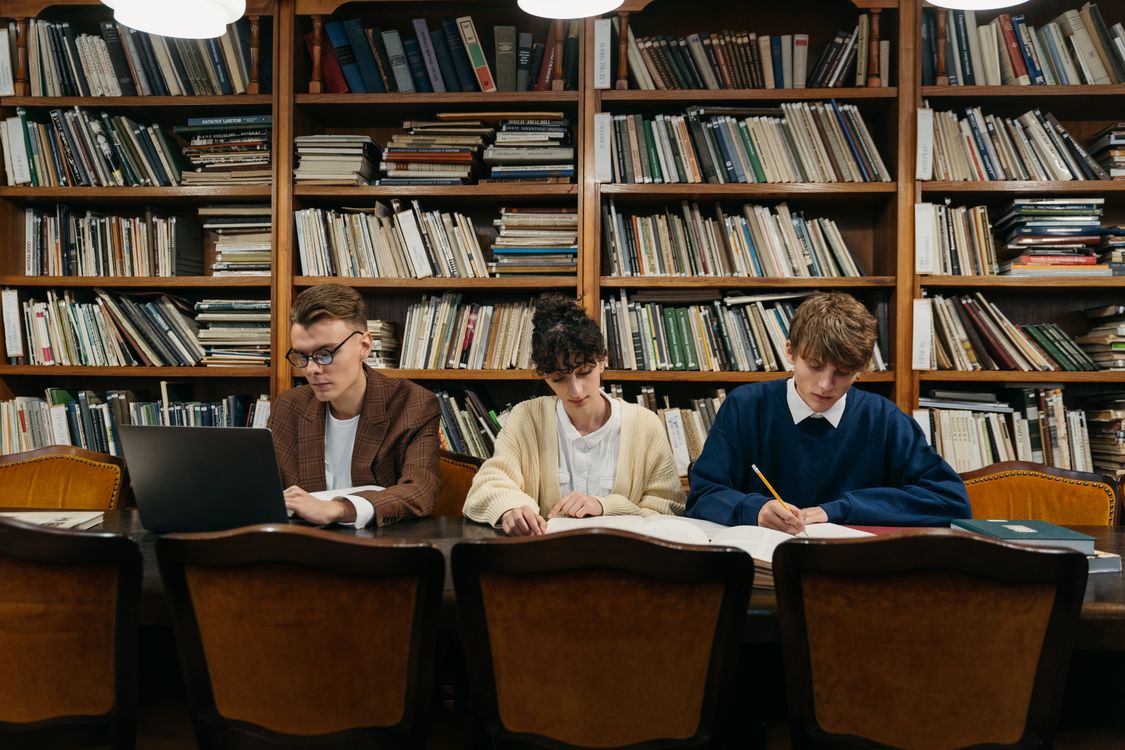 Three college students collaborating on research in an academic library setting