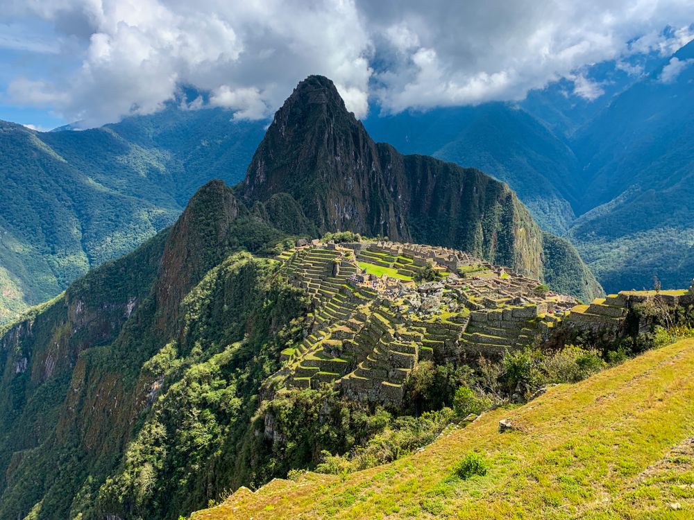 Green and brown Andean mountains surrounding Machu Picchu under white clouds near Cusco