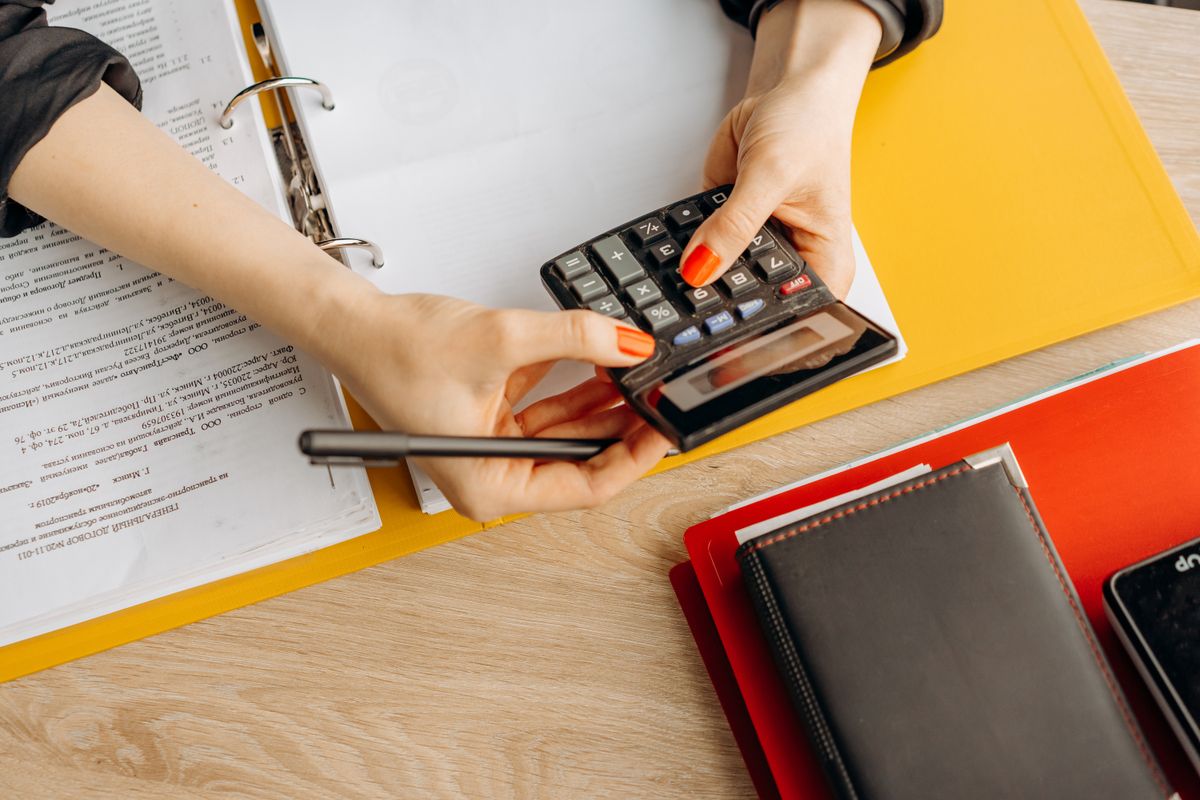 Woman using a calculator at a desk with documents and folders for small business financial planning