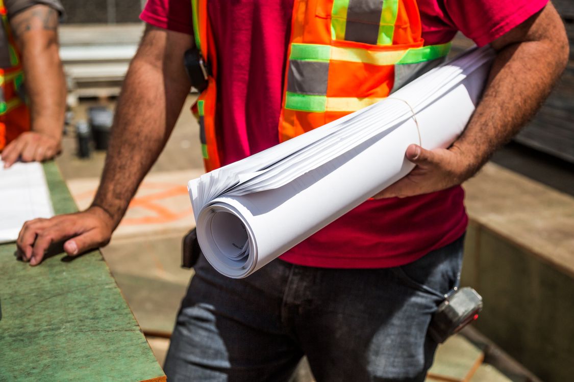 Two construction workers in safety vests reviewing building blueprints together