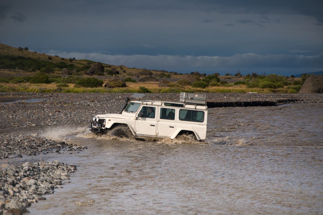 White 4x4 crossing a rocky river in Iceland's highland landscape